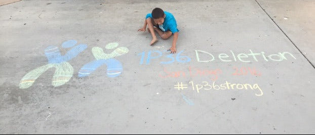 Noah drawing on pavement with colorful chalk, including text '#1p36Deletion' and '#1p36Strong'.