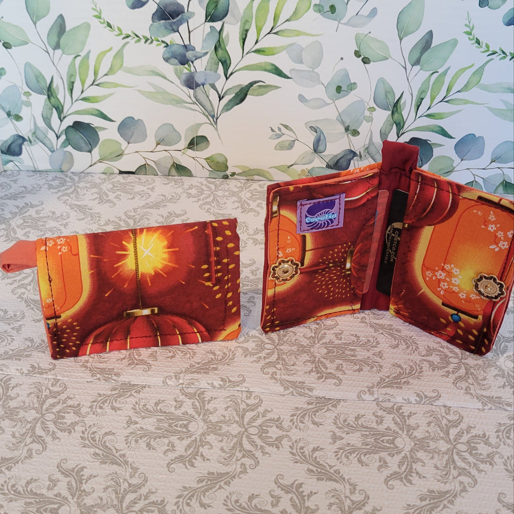Orange Lantern Design Wallet on red fabric. Standing on top of a crazy lace design and a leave pattern background.