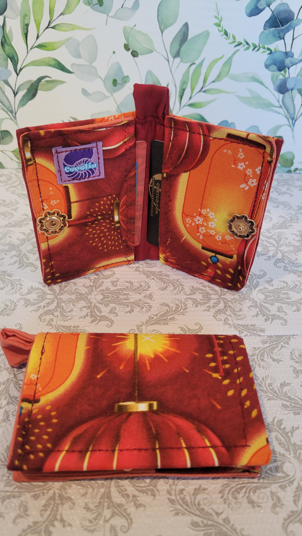 A wallet with a vibrant pattern of red and orange lanterns, displayed both closed and open, showing its interior compartments.