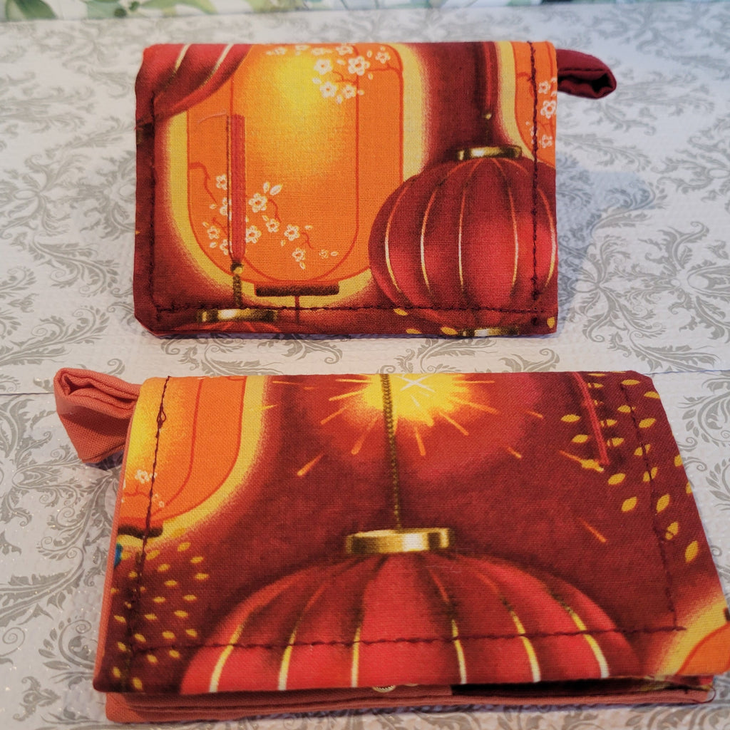 Orange Lantern Design Wallets on red fabric. Standing on top of a crazy lace design.