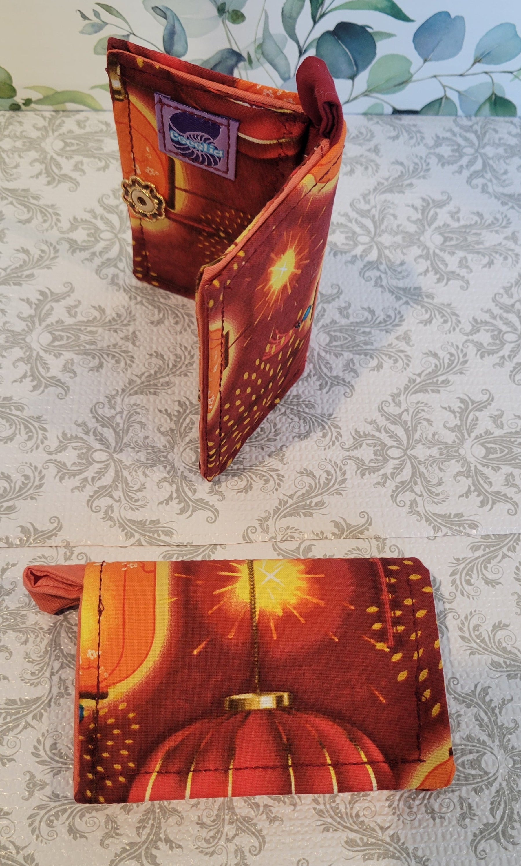 Orange Lantern Design Wallet on red fabric. Standing on top of a crazy lace design and a leave pattern background.