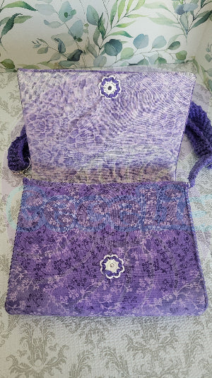 Purple florals patten clutch purse on a textured surface. Attach is two sliver hook and adjustable crochet strap in purple.