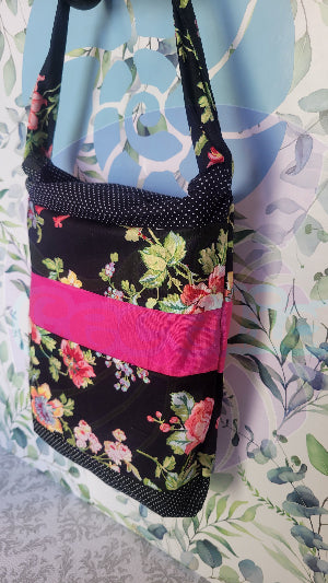 A black Angelica purse with a pink floral pattern and a hot pink and white polka-dots on black fabric stripe, displayed against a floral background.
