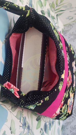 Floral-patterned bag with a pink interior and a hard cover book on a floral background