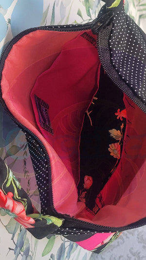 Close-up of A black Angelica purse with a pink floral pattern and a hot pink and white polka-dots on black fabric stripe, displayed against a floral background. Inside is a pink and black pocket.