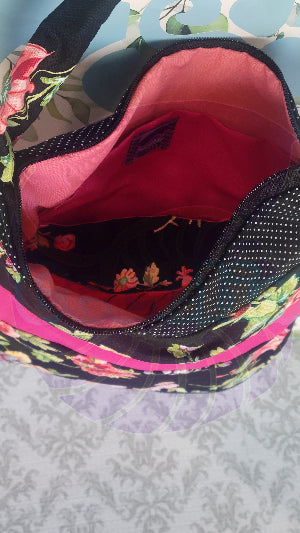 Close-up of a black Angelica purse with a pink floral pattern and a hot pink and white polka-dots on black fabric stripe, displayed against a floral background.and pink interior.