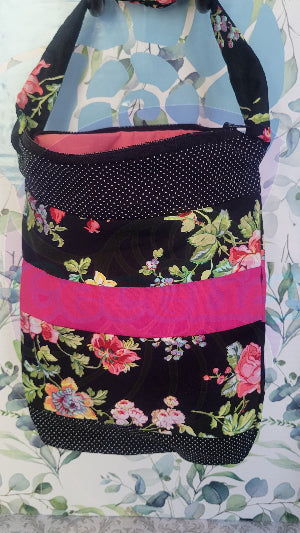 A black Angelica purse with a pink floral pattern and a hot pink and white polka-dots on black fabric stripe, displayed against a floral background.