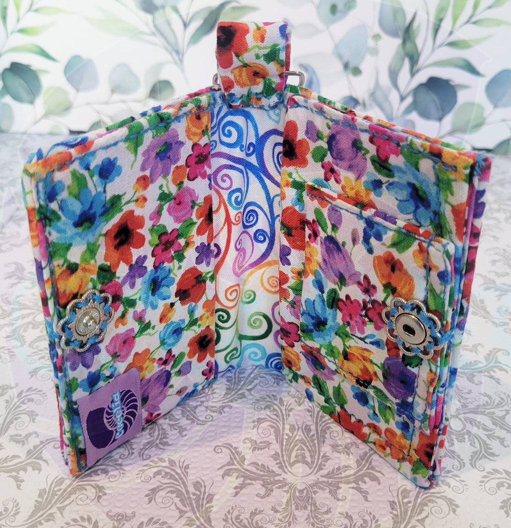 Multicolored floral-wallet pouch with a keychain on a white lace background. Open to show one pocket on each side of the wallet.
