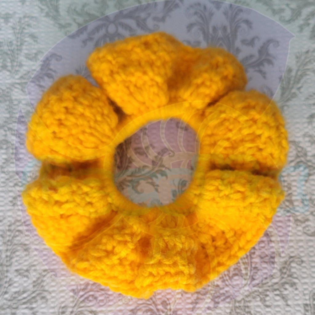 Crocheted yellow scrunchie on a blue and patterned surface