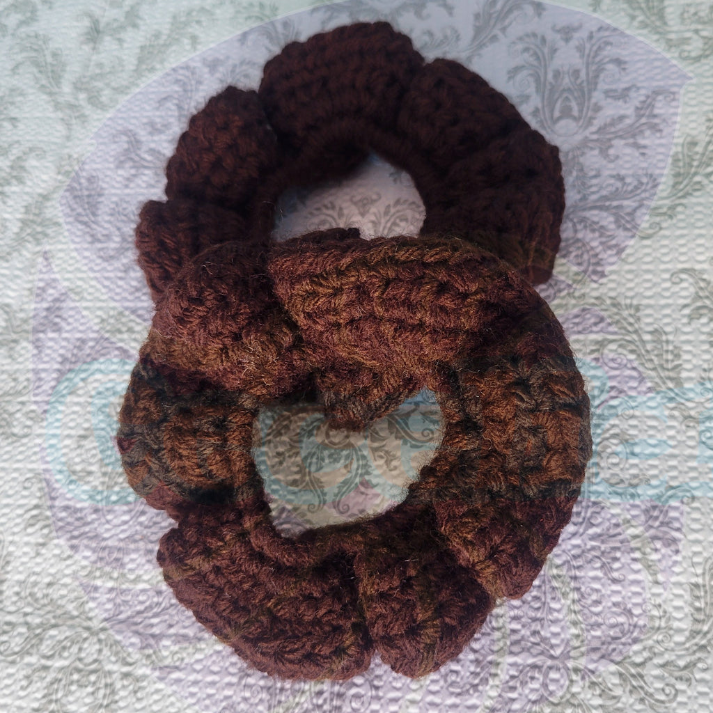 two brown crocheted scrunchies on a textured fabric background