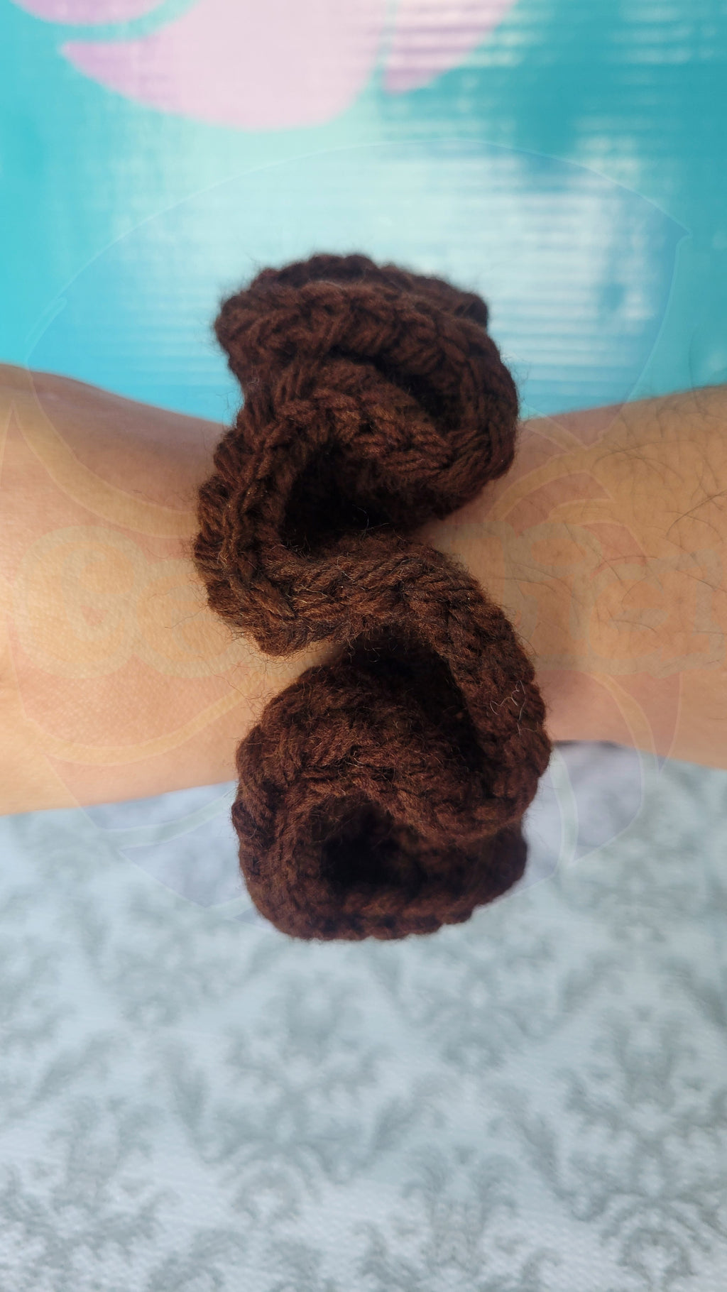 Brown crochet scrunchie on a wrist with a blue and pink background