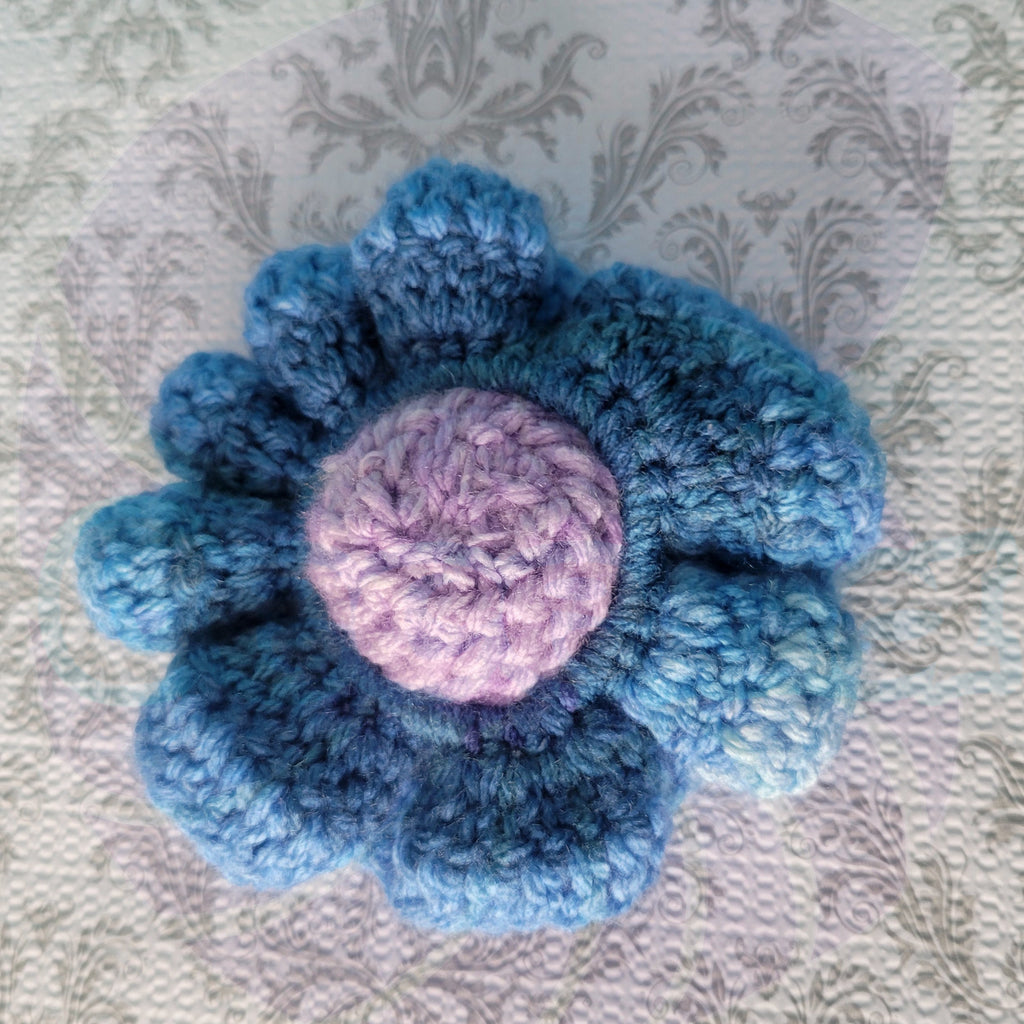Blue gradient crocheted scrunchies in a purple ball center on a textured fabric background