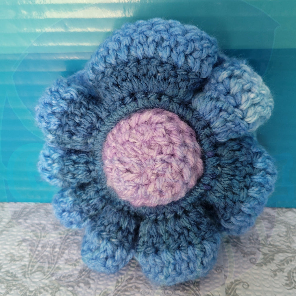 Blue gradient crocheted scrunchies in a purple ball center on a textured surface with a blue background