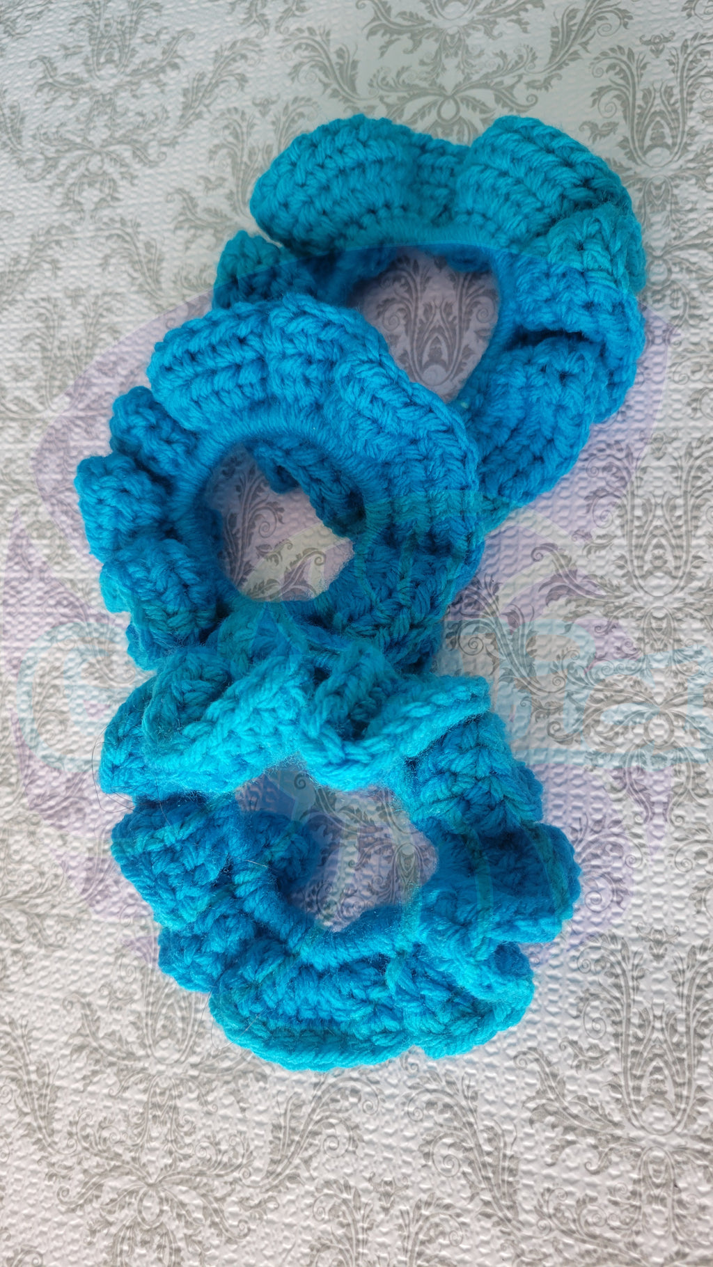 three Blue crayon crocheted scrunchie on a textured gray background