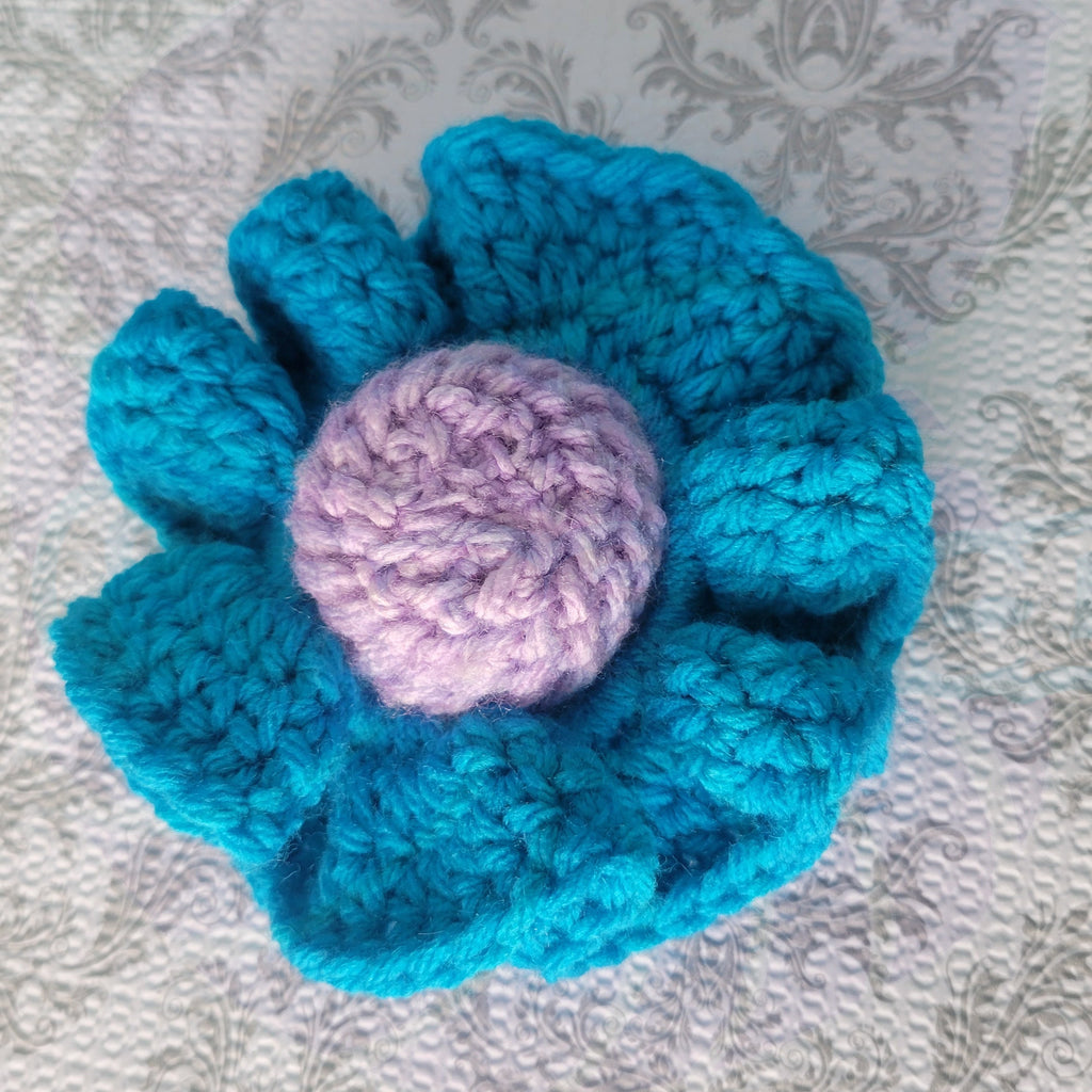 a crocheted scrunchie with blue ball and a pink center on a textured gray background