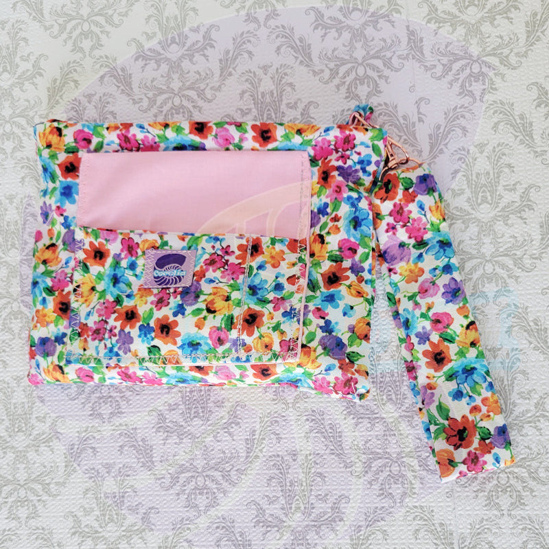 colorful Floral-patterned pouch purse in white with a light pink pocket on a textured white background. Attach to a pink metal hook is the hand size strap.