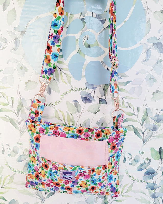 colorful Floral-patterned pouch purse in white with a light pink pocket on a textured white background. Attach to a set of pink metal hooks is the adjustable strap.