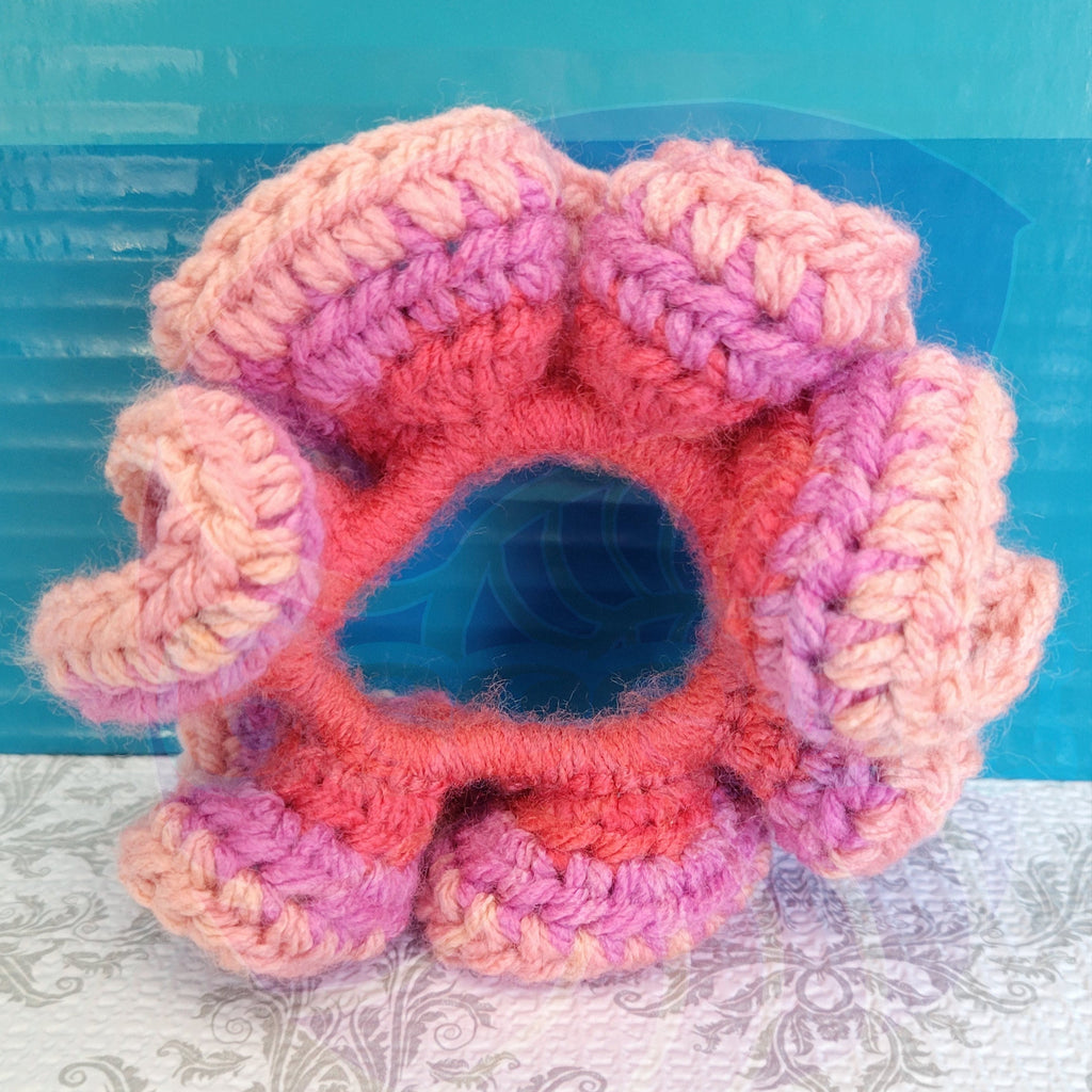Crocheted pink and orange scrunchie on a textured surface with a blue background