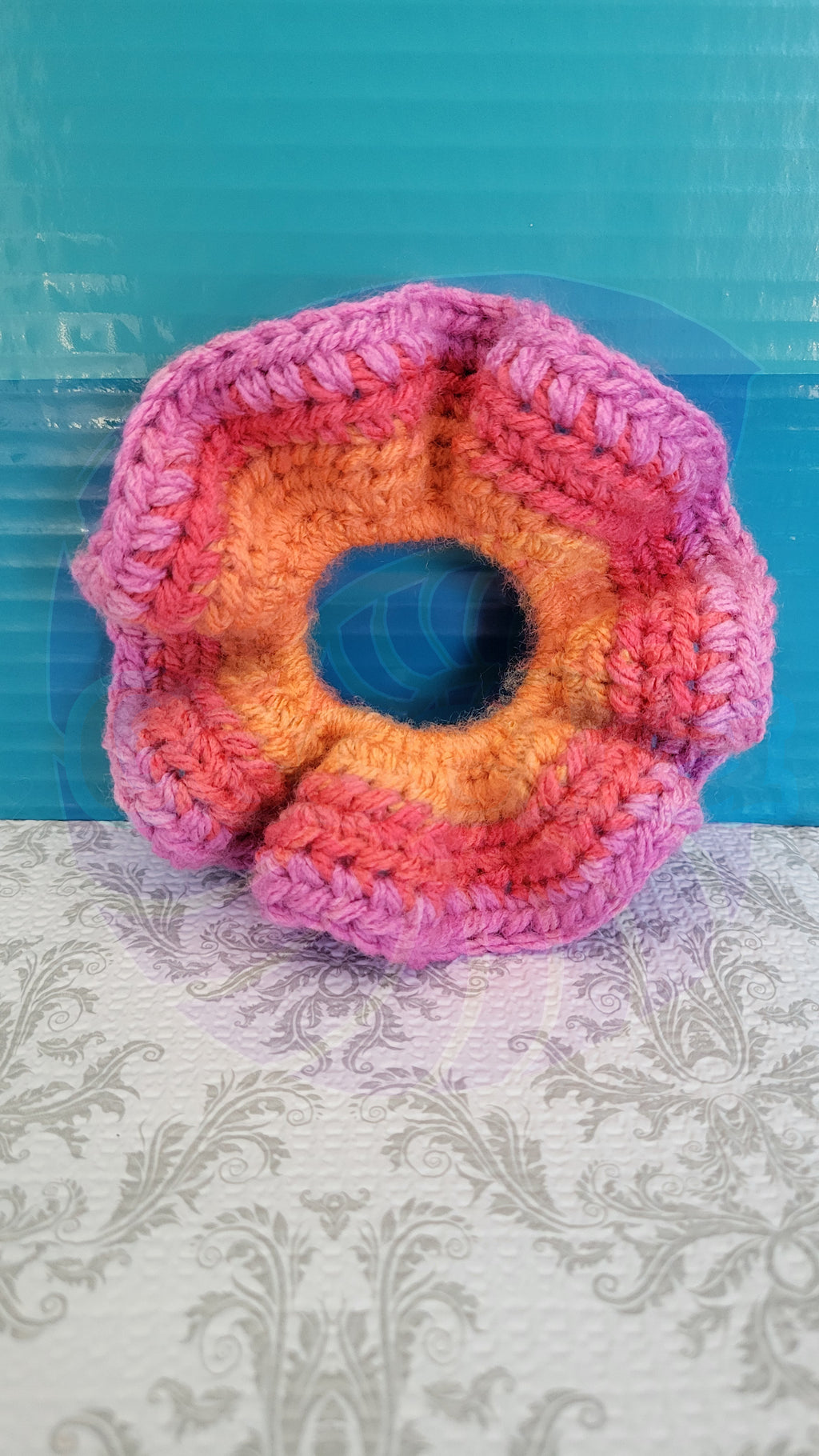 Colorful crocheted scrunchie on a textured surface with a blue background