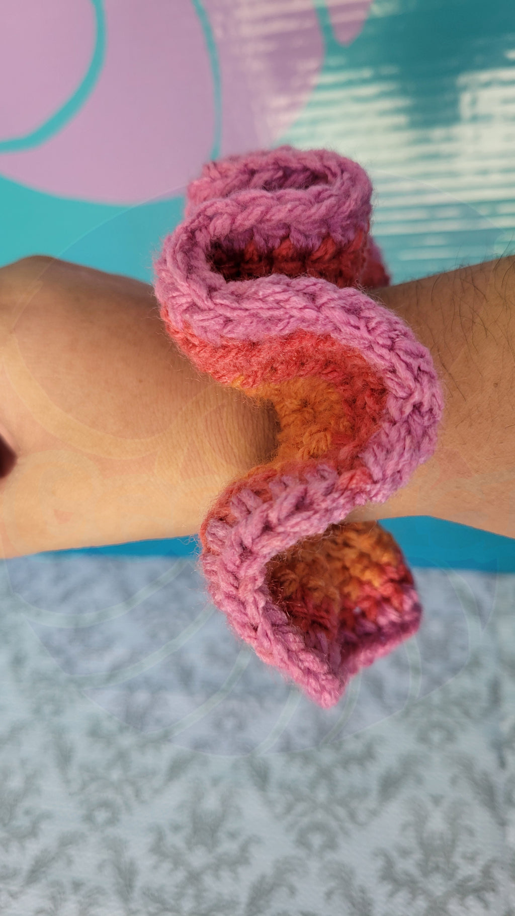 Pink, orange and red crochet scrunchies on a wrist with a colorful background