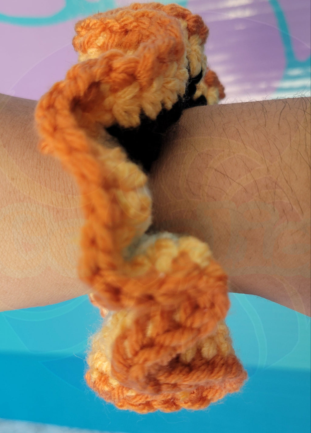 several shades of orange, black and white scrunchie  on a wrist with a colorful background