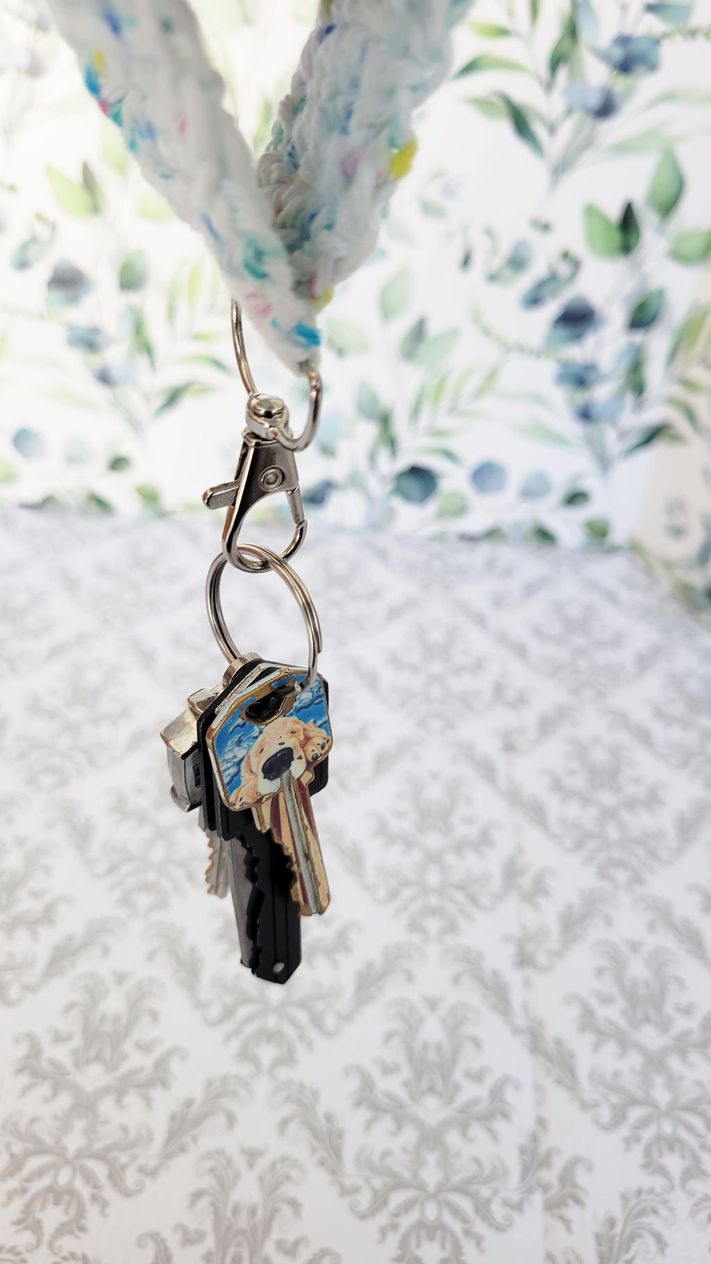 Keychain with keys attached to a crochet lanyard of white with colorful sparkles against a floral background
