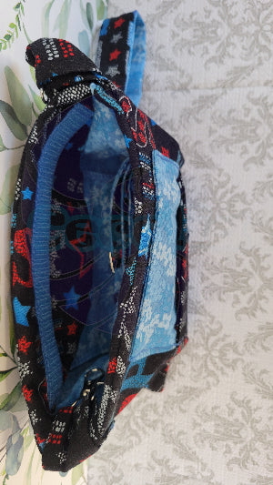 the crossbody of a small purse with the words USA and blue verco opening. Outside is a floral blue pocket and the purse is attached by two sliver hooks on the side and an adjustable strap in the same fabric. This picture is a close up on inside the purse with another floral blue pocket.