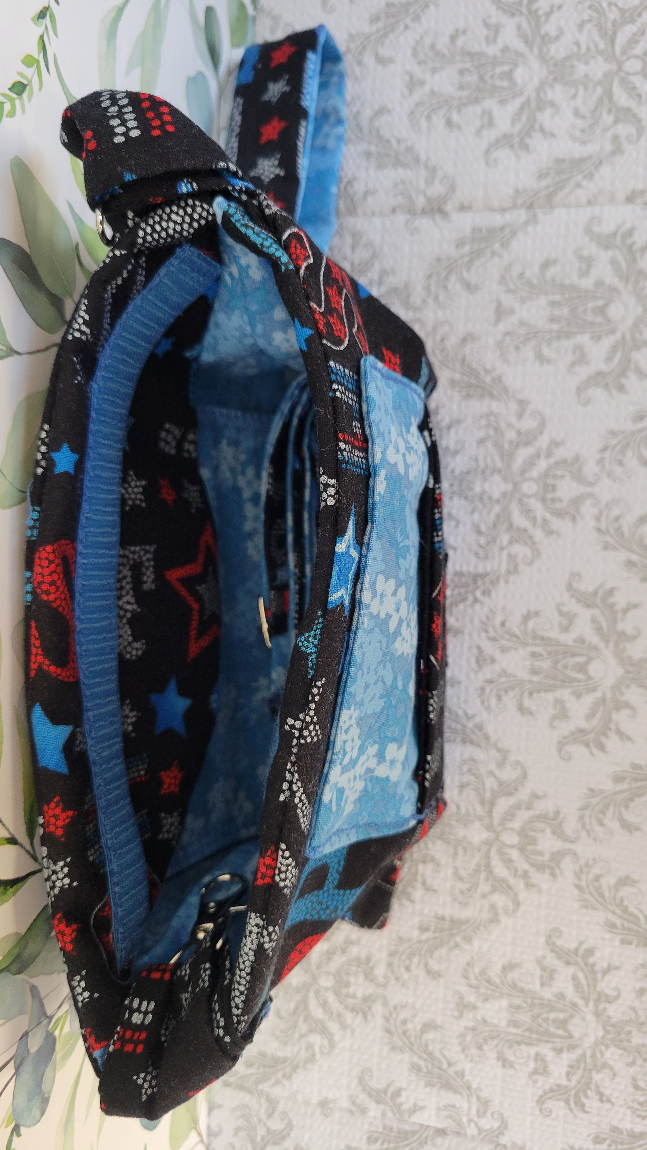 A purse shown from above on a light patterned surface. The exterior has a black base with blue, red, and white star and dot patterns, and the interior is lined in blue.