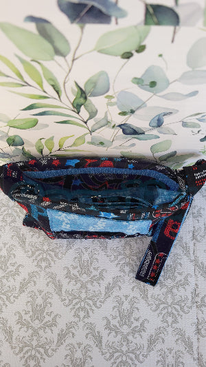 the crossbody of a small purse with the words USA and blue verco opening. Outside is a floral blue pocket and the purse is attached by two sliver hooks on the side and an adjustable strap in the same fabric.