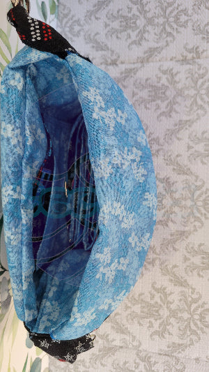 the crossbody of a small purse with the words USA and blue verco opening. Outside is a floral blue pocket and the purse is attached by two sliver hooks on the side and an adjustable strap in the same fabric.