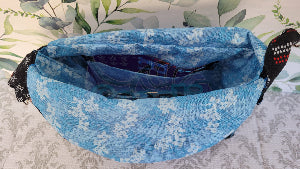 the crossbody of a small purse with the words USA and blue verco opening. Outside is a floral blue pocket and the purse is attached by two sliver hooks on the side and an adjustable strap in the same fabric.
