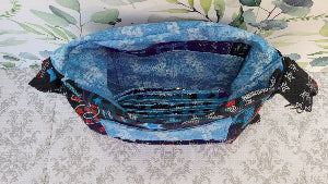 the crossbody of a small purse with the words USA and blue verco opening. Outside is a floral blue pocket and the purse is attached by two sliver hooks on the side and an adjustable strap in the same fabric.