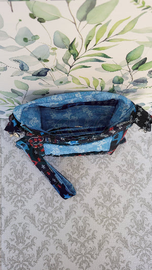 the crossbody of a small purse with the words USA and blue verco opening. Outside is a floral blue pocket and the purse is attached by two sliver hooks on the side and an adjustable strap in the same fabric.