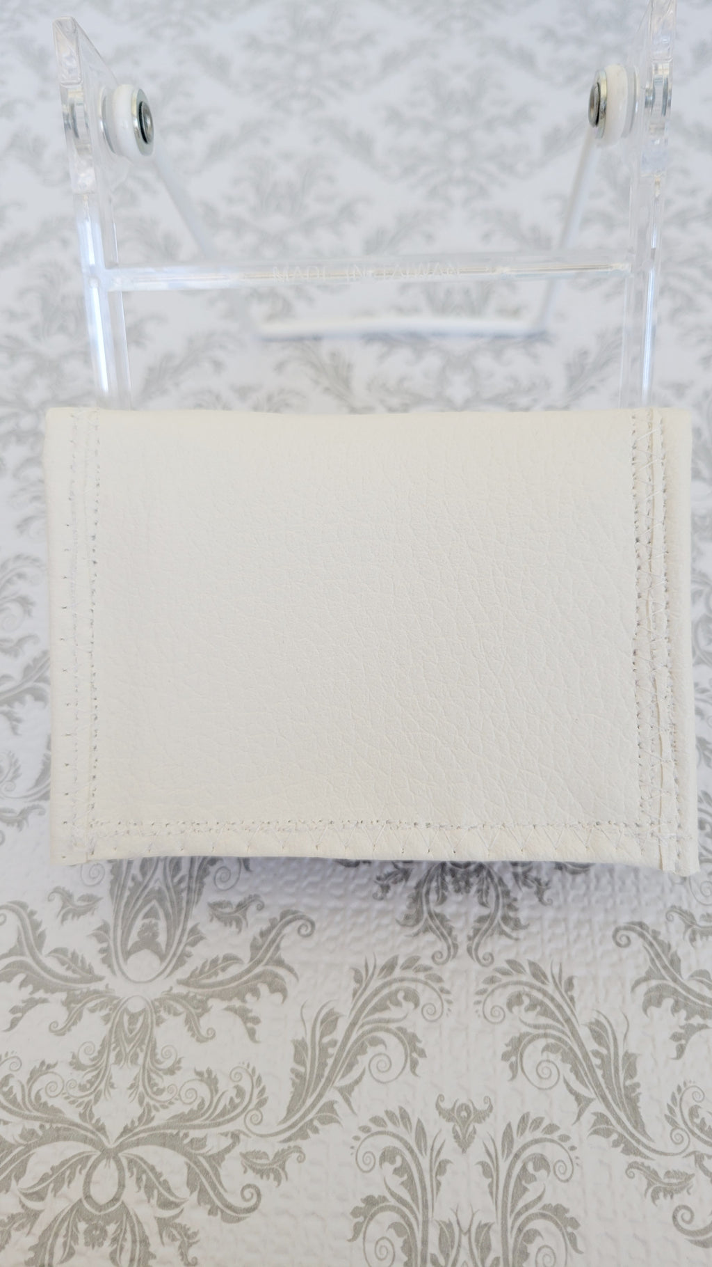 White wallet hanging on a silver frame holder against a patterned wall.