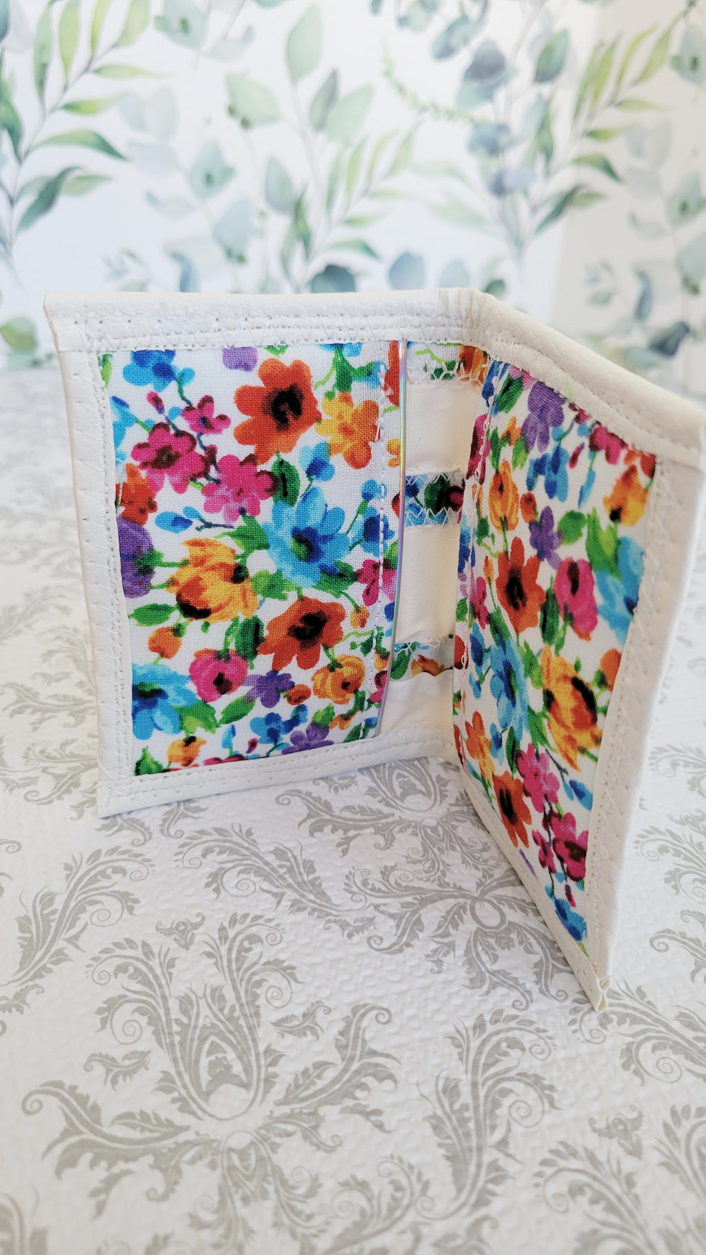 Open book position of a wallet with colorful floral pattern on a decorative background. Inside you see one pocket on each side.