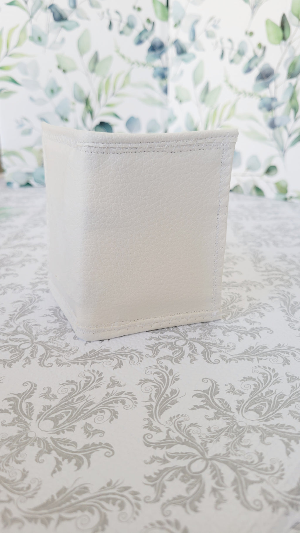 White wallet standing up on a patterned surface with a floral background