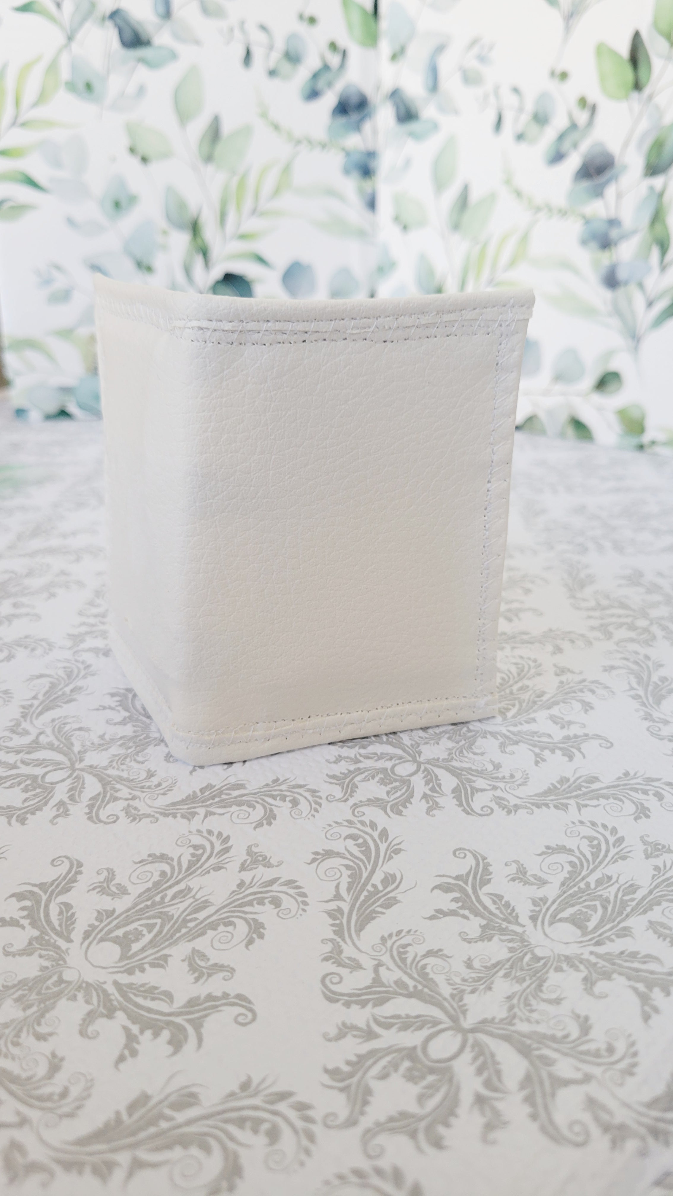 White wallet standing up on a patterned surface with a floral background
