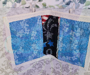 Quilted fabric wallet with blue floral pattern and black fabric with american flag design on a floral background. There are two pocket is floral blue color.