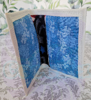 Quilted fabric wallet with blue floral pattern and black fabric with american flag design on a floral background. There are two pocket is floral blue color.