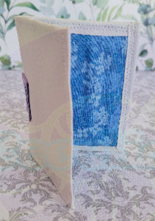 Quilted fabric wallet with blue floral pattern and black fabric with american flag design on a floral background. There are two pocket is floral blue color. Outside color is white with the company logo.