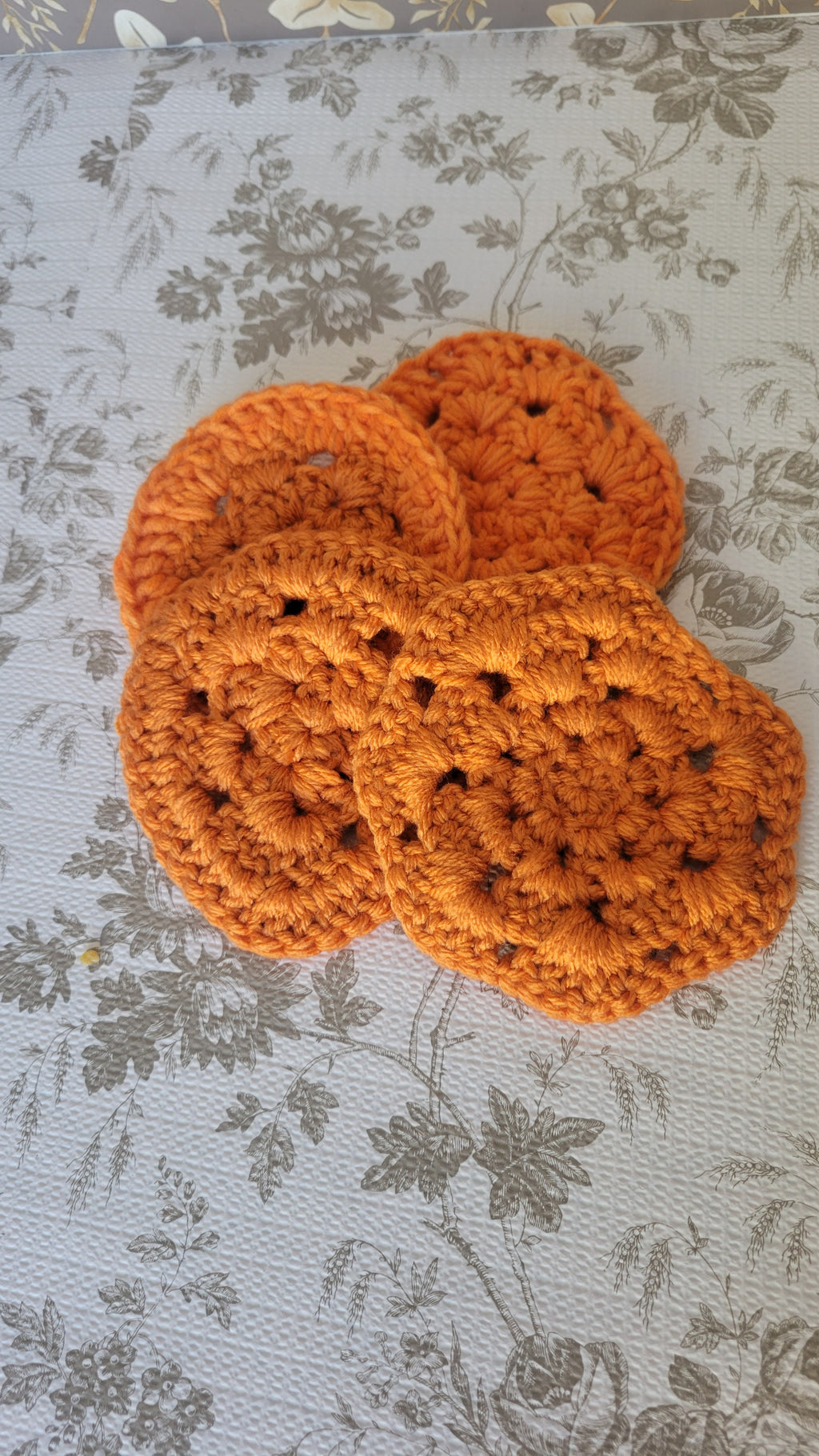Four orange crocheted coasters in the shape of a circle on a white patterned surface