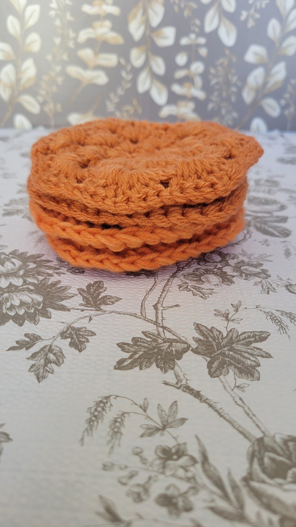 Four orange crocheted coasters in a stack on a white patterned surface