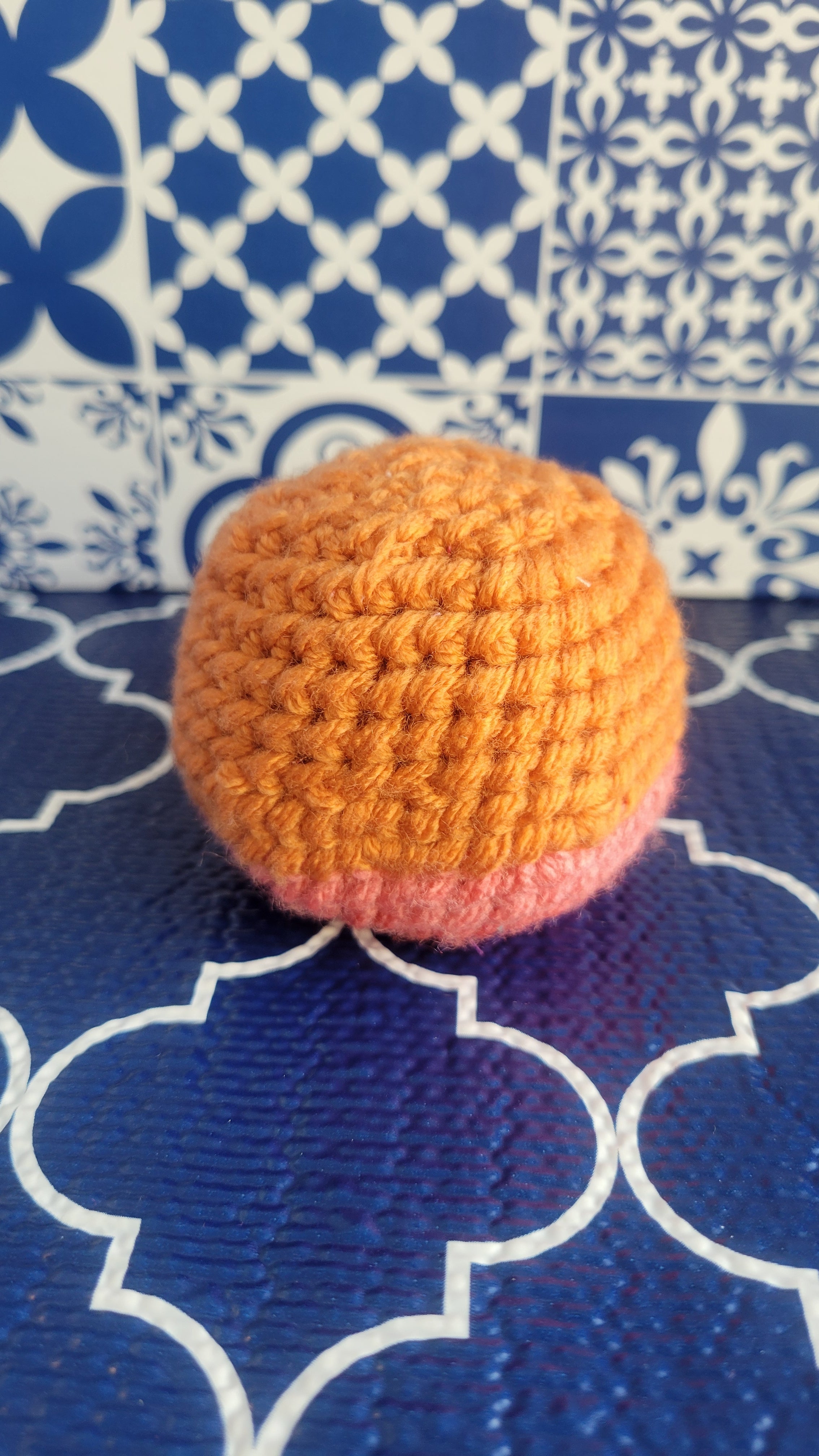 Crocheted orange and pink stress ball on a blue and white patterned fabric background