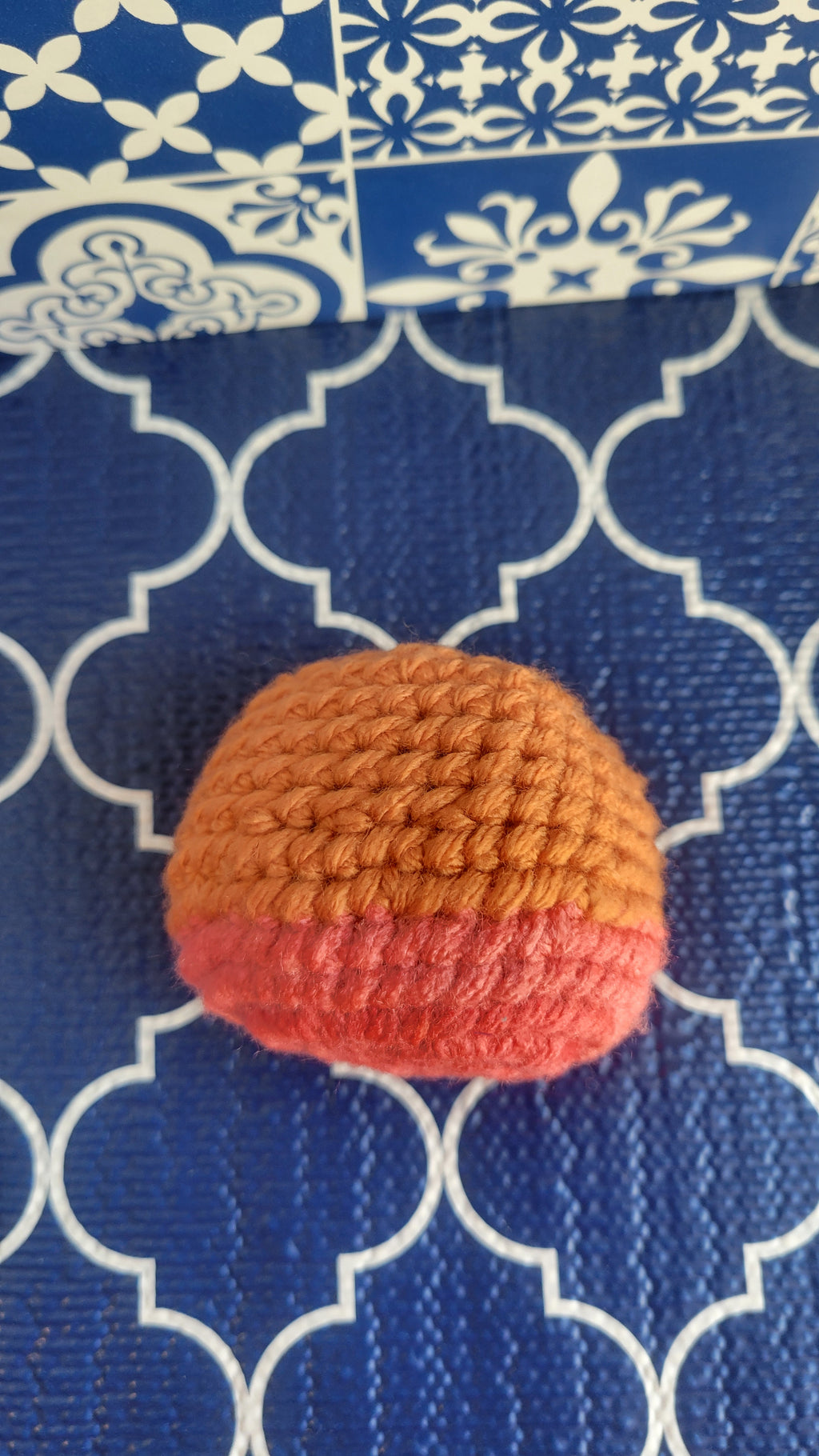 Crocheted orange and pink stress ball laying on a blue and white patterned fabric background