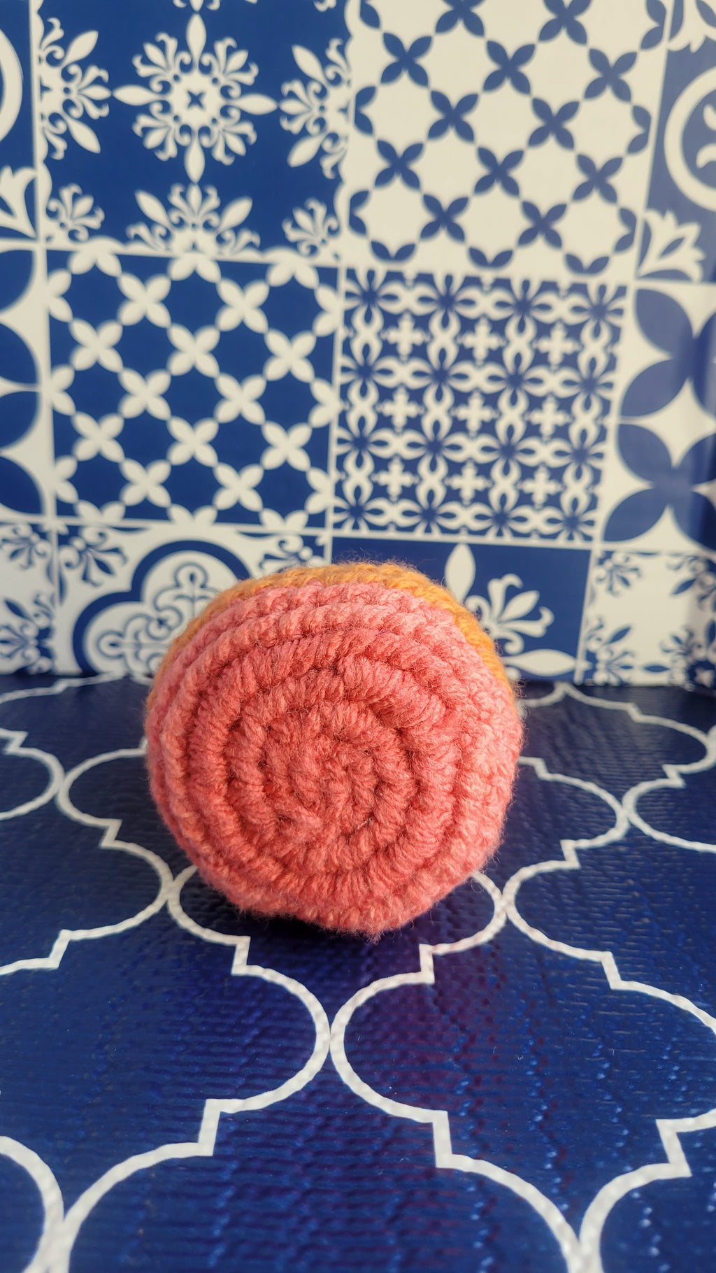 Close-up of a crochet pink circular stress ball on a blue and white patterned fabric background
