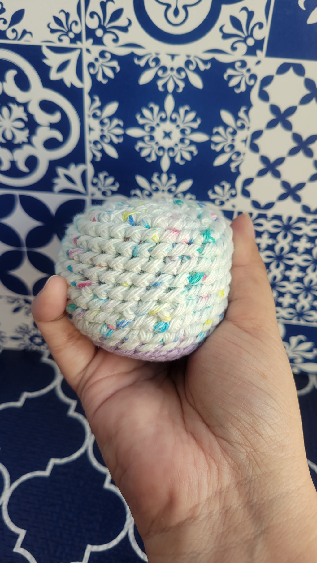 Hand holding a white stress ball with different color sprinkles against a blue and white patterned background