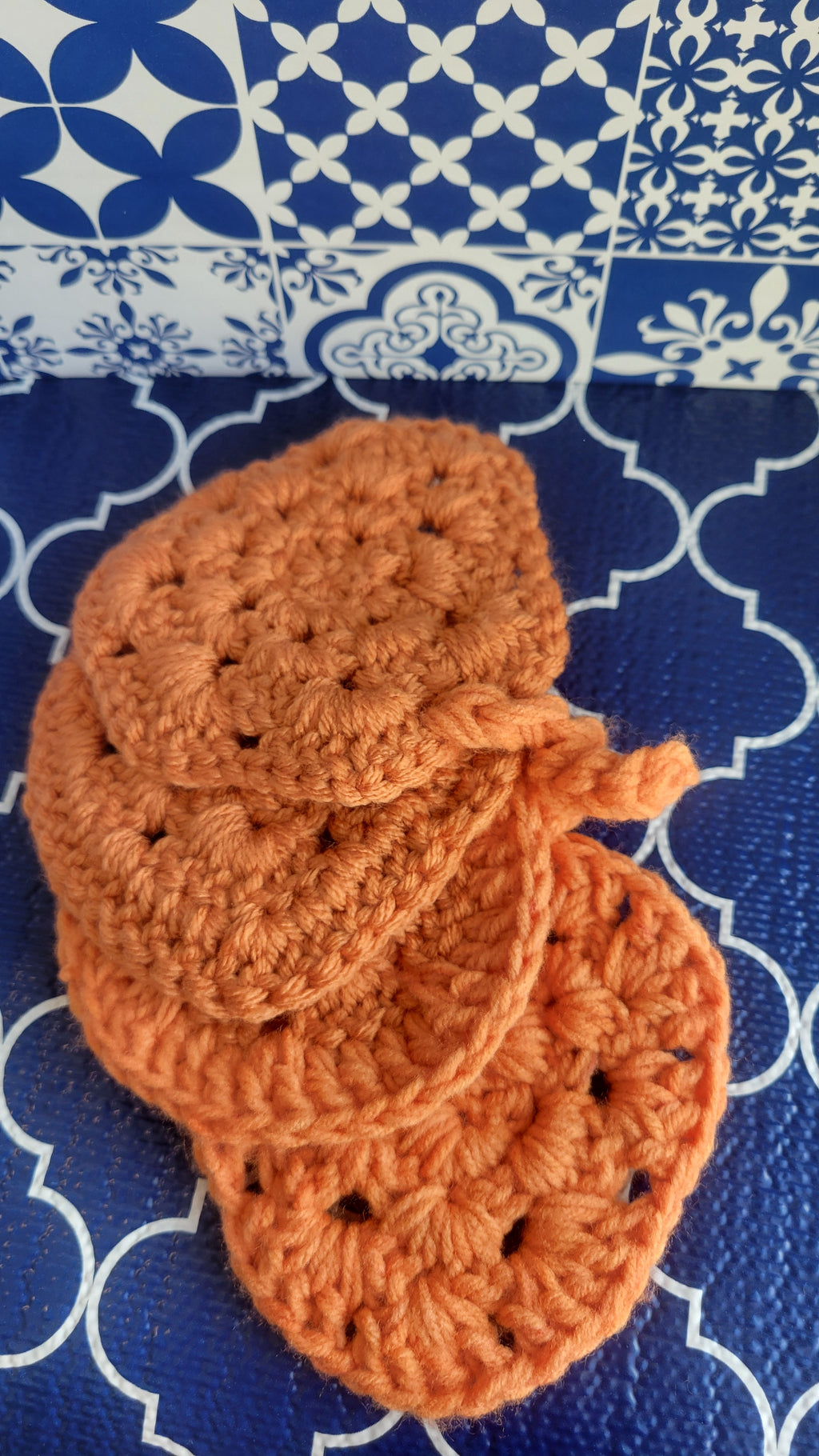 Four orange crocheted coasters in the shape of a pumpkin on a blue and white patterned surface