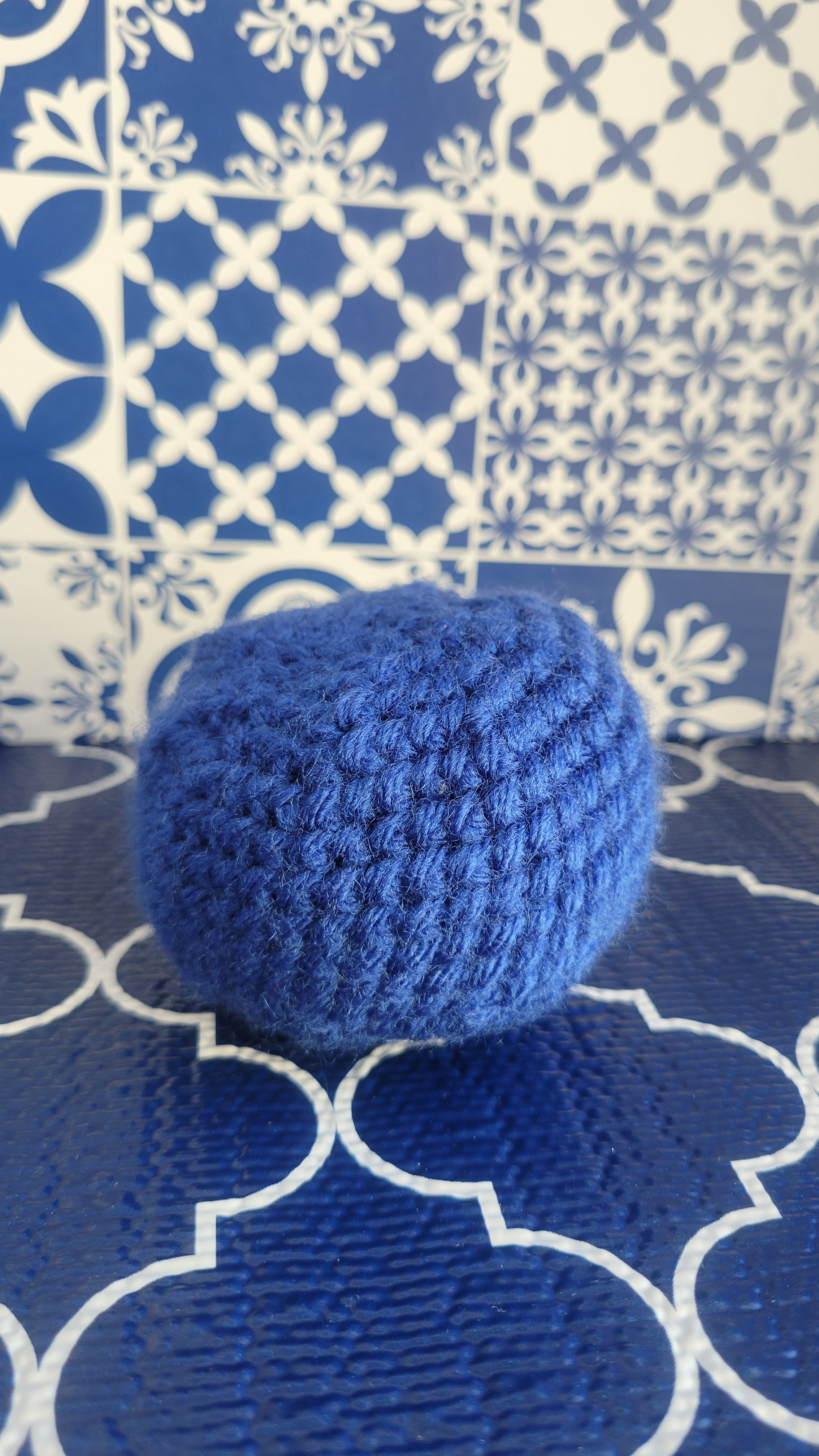 Royal Blue Stress Ball made of crochet cotton yarn. Background is Spanish tiles in blue and white desgin curves on blue floor.