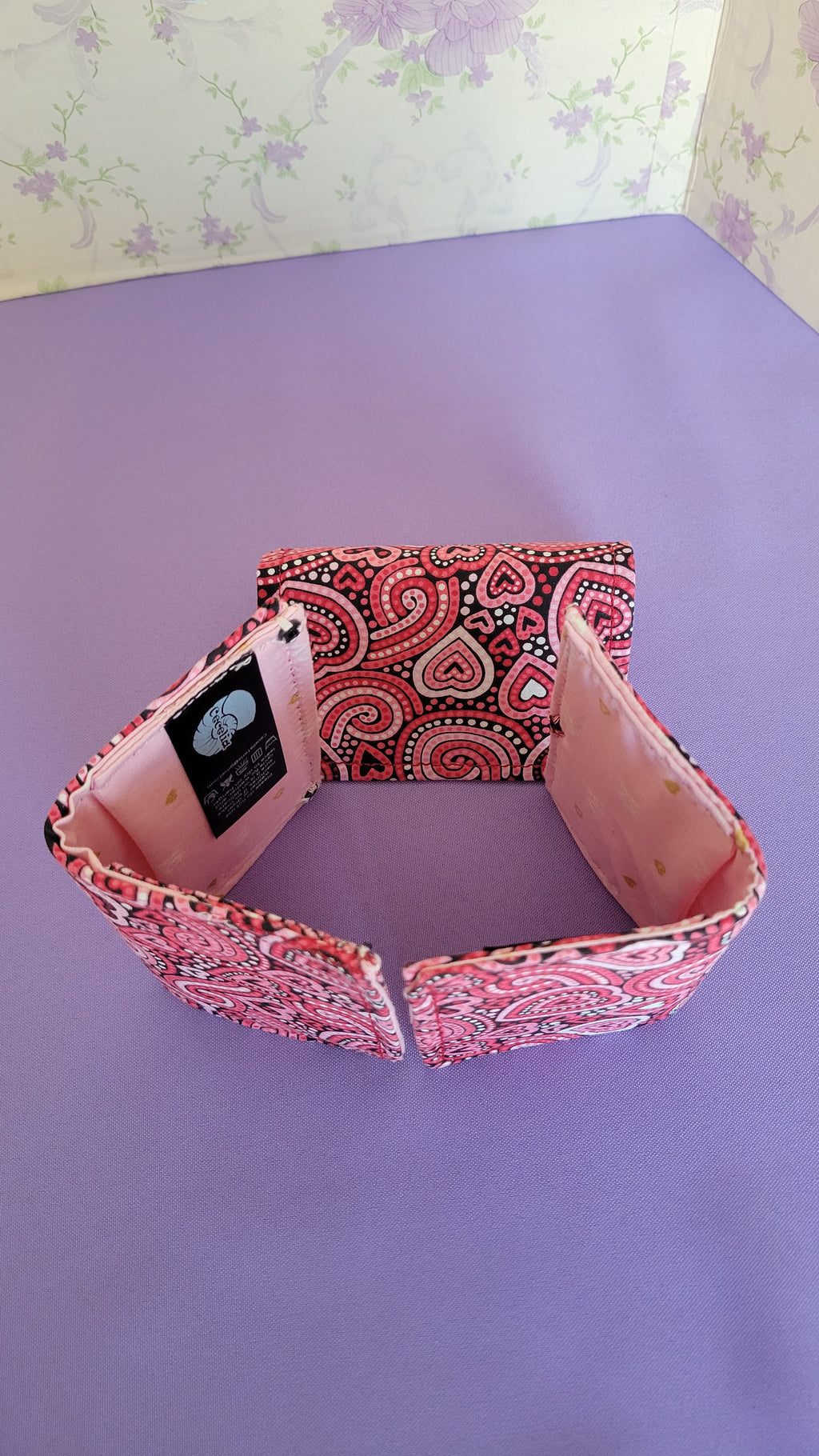 Three Javier wallets with a ripple effect of hearts in a selection of colors pink, white, red and black. They are placed together to make a box.
