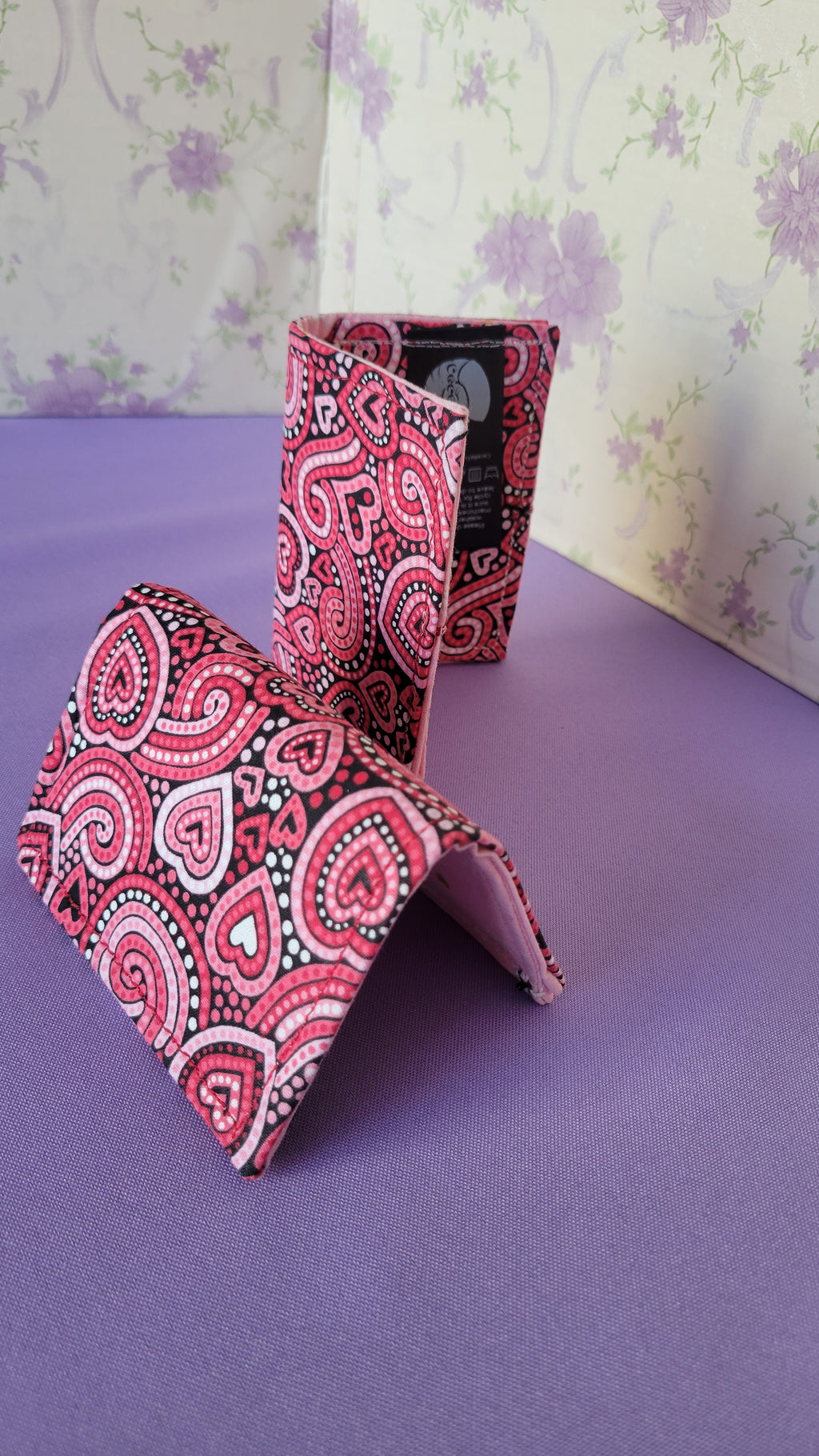 Three Javier wallets with a ripple effect of hearts in a selection of colors pink, white, red and black. They are placed parallel with one on a turning table.